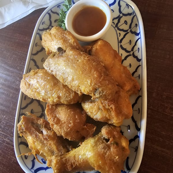 Golden-brown fried chicken wings with a side of dipping sauce on a patterned Thai Palace plate.