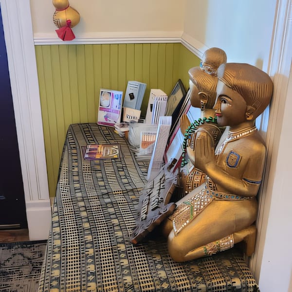 Golden Thai statues with hands pressed together in prayer, next to a patterned table and green wall.