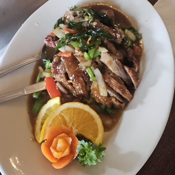 Crispy duck in brown sauce with vegetables, garnished with orange slices and a carrot flower.