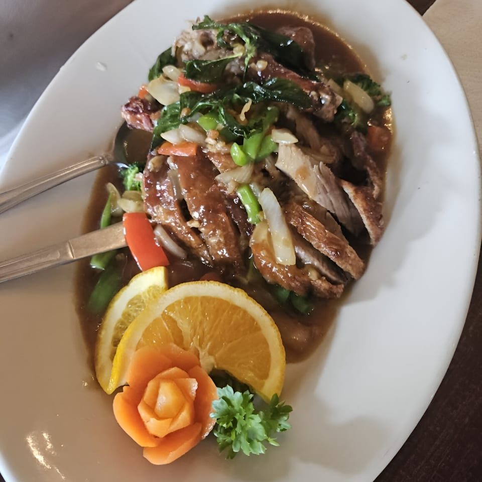 Crispy duck in brown sauce with vegetables, garnished with orange slices and a carrot flower.