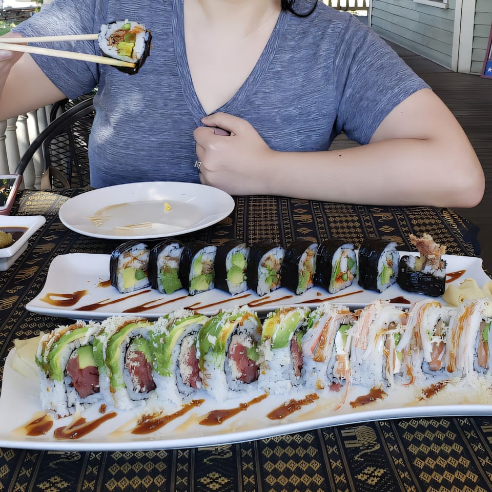 A person holds a sushi roll with chopsticks over two plates of sushi rolls at Thai Palace.