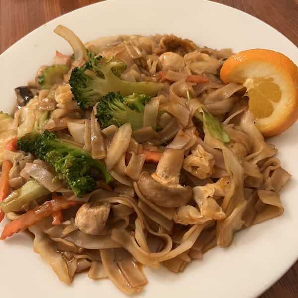 Thai Palace & Sushi Bar's Pad See Ew with wide noodles, broccoli, carrots, mushrooms, and an orange slice.