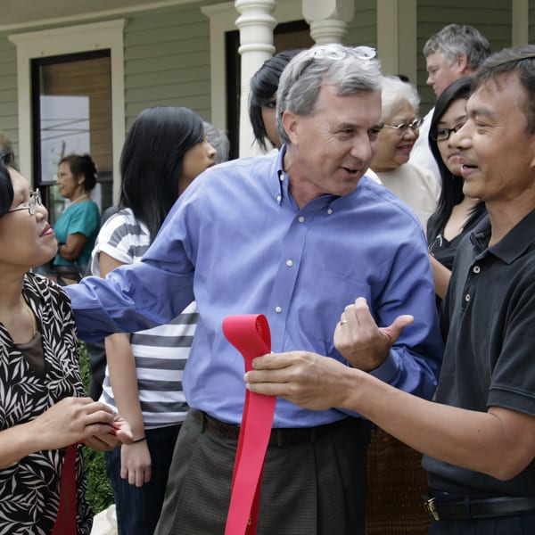 A man in a blue shirt holds a red ribbon with another man, surrounded by people.