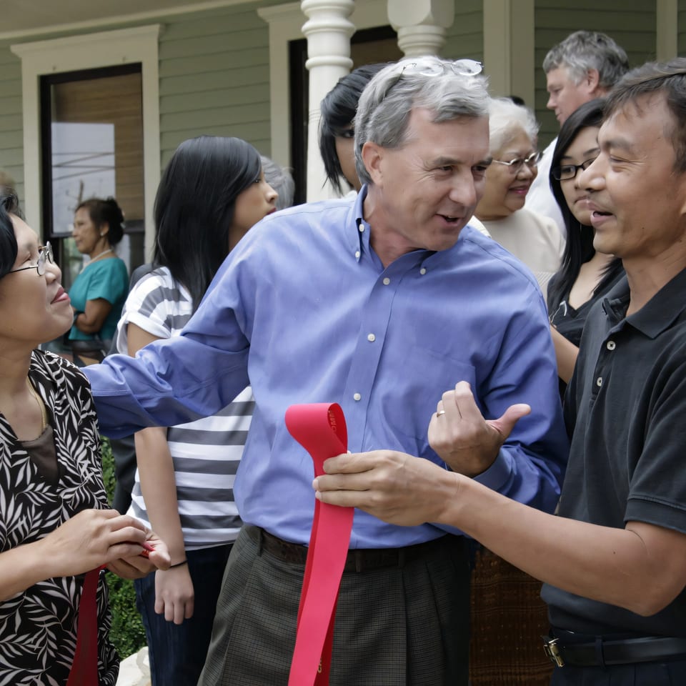 A man in a blue shirt holds a red ribbon with another man, surrounded by people.