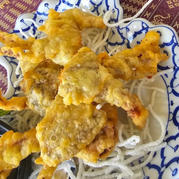 Crispy fried soft-shell crab tempura served on a bed of white vermicelli noodles in a blue and white bowl.