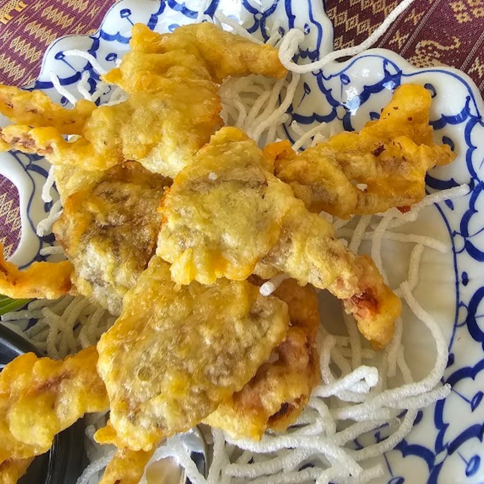 Crispy fried soft-shell crab tempura served on a bed of white vermicelli noodles in a blue and white bowl.