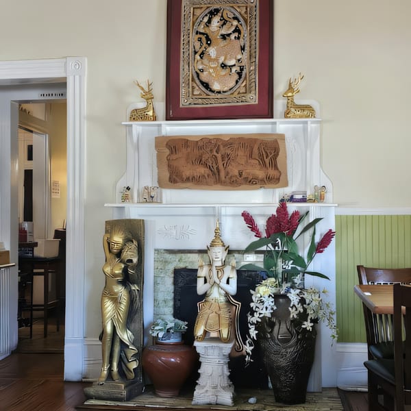 Thai Palace & Sushi Bar's interior features a fireplace adorned with Thai statues, carvings, and red ginger flowers.