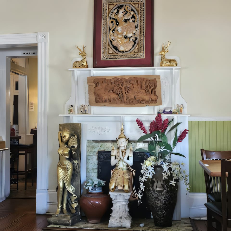 Thai Palace & Sushi Bar's interior features a fireplace adorned with Thai statues, carvings, and red ginger flowers.