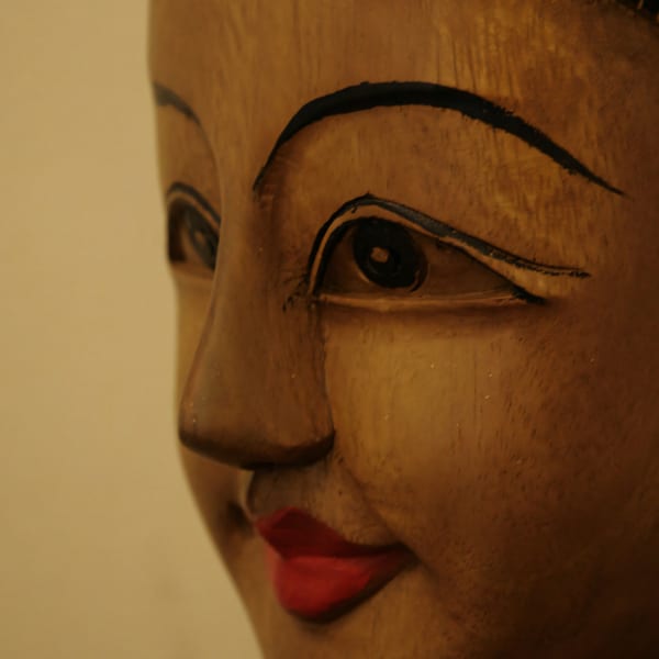 Close-up of a wooden Thai sculpture with black eyebrows and red lips.