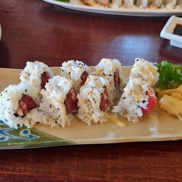 Sushi rolls with white rice, tuna, sesame seeds, and a creamy sauce, served on a decorative plate.